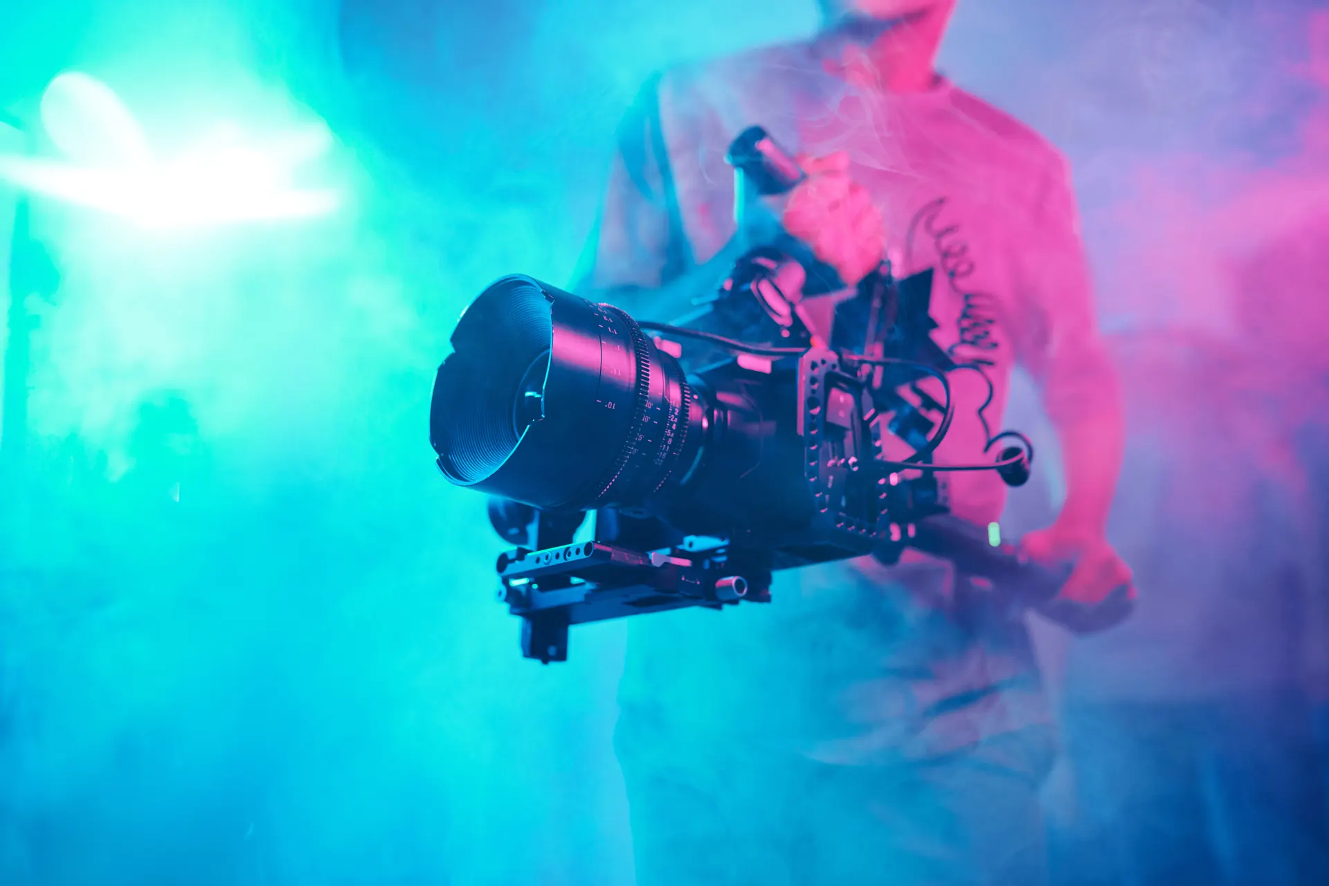 Kameramann hält eine Cinema Kamera mit Cine Objektiv an einem Handrig im farbigen Bühnennebel
